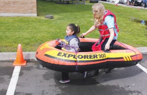 By Greg Farrar Tanya Arriaga, 6, leads Coal Creek Family YMCA staff employee Carter Bolomey through the aquatics obstacle course in the parking lot during the free Healthy Kids Day community event April 25 in Newcastle. Children learned about wearing life vests and other aspects of water safety in the exercise. Hundreds of youngsters with their families took part in relay races, rock wall climbing, dodgeball games, miniature golf and inflatable obstacle bounce house attractions. View more photos at http://on.fb.me/1JVGREy.