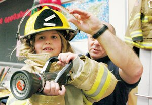By Greg Farrar Above, at left, Chloe Brousseau, Hazelwood Elementary School first-grader, gets a huge kick out of wearing a child-sized set of bunker gear and holding a fire hose nozzle as Eastside Fire & Rescue firefighter Tim Castner adjusts her helmet on Career Day.